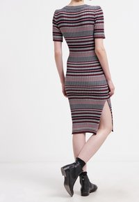 Randig stickad klänning med korta ärmar, med en sidoslits, i nyanser av grått, vinröd och vitt. Bärs med svarta ankelstövlar.