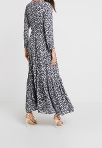 Bloemen maxi-jurk in marineblauw met witte bloemen, lange mouwen, een aansluitende taille en een gelaagde, uitlopende zoom. Draag met beige haksandalen.