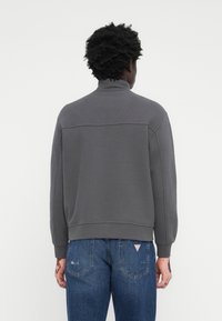 Sweatshirt gris avec un col montant, des poignets et un ourlet côtelés. Le tissu semble doux et texturé. Porté avec un jean en denim bleu.