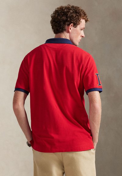 Κόκκινο πόλο πουκάμισο με γιακά σε ναυτικό μπλε και μανσέτες στα μανίκια, κατασκευασμένο από βαμβάκι, με κεντημένη λεπτομέρεια στο μανίκι.