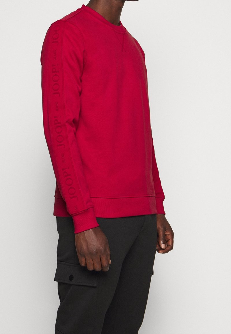 Sudadera roja con puños y dobladillo acanalados, que presenta un branding en relieve oscuro "JOOP!" a lo largo de las mangas; tejido de mezcla de algodón, corte regular.