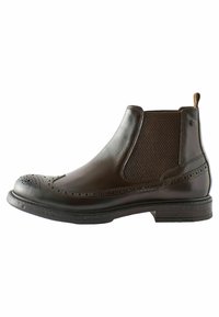 Brun læder ankelstøvle med brogue-detaljer, elastiske side_paneler, tekstureret materiale og en robust gummisål.