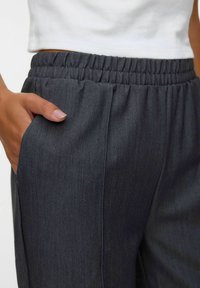 Pantalons gris à taille élastique avec poches latérales, présentant un tissu texturé et une coupe décontractée, agrémentés de plis subtils pour une touche de détail.