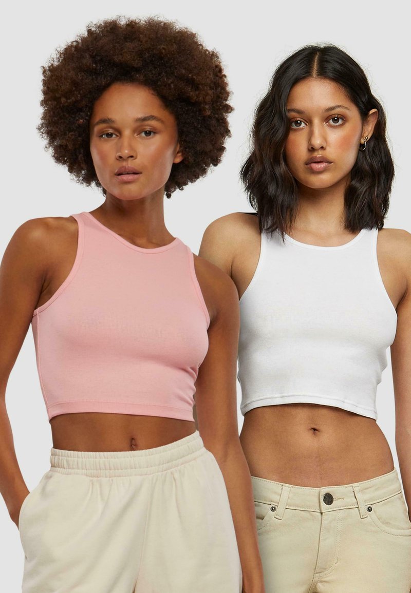 Zwei gekürzte Tanktops: eines in zartem Rosa, das andere in Weiß. Beide haben ein ärmelloses Design, einen runden Ausschnitt und eine gerippte Textur.