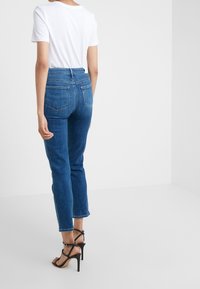 Korkeavyötä Blue farkut, joissa on kapeneva lahje, takataskut ja siisti viimeistely, yhdistettynä istuvaan valkoiseen T-paitaan.