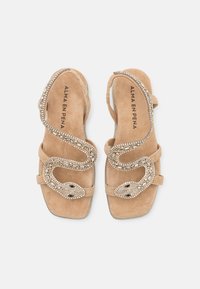 Beige suède sandalen met een slangenontwerp en rhinestone versieringen met zwarte oogaccenten. Open teen met een verstelbaar bandje.