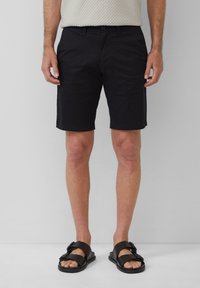 Schwarze Baumwollshorts mit geradem Schnitt, ausgestattet mit einem Knopfverschluss und seitlichen Taschen, kombiniert mit schwarzen Sandalen. Glatte Stofftextur.