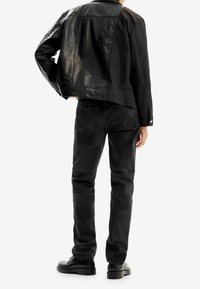 Giubbotto in pelle nera con finitura opaca, abbinato a jeans scuri a toppe e scarpe nere stringate, visto da dietro.