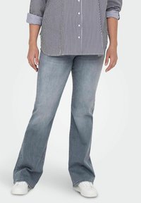Jeans de campana grises de denim, con un acabado desgastado. Se combinan con una camisa de botones a rayas en blanco y negro y zapatillas blancas.