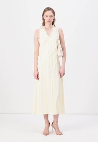 Rochie crem cu bretele, cu decolteu în V și accente plisate, având un design tip wrap și o siluetă fluidă, de lungime medie.