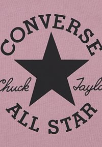 Ροζ ύφασμα με μεγάλο μαύρο αστέρι. Το κείμενο γράφει "CONVERSE" σε τόξο πάνω και "Chuck Taylor ALL STAR" κάτω σε έντονη γραμματοσειρά.
