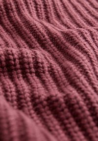 Gros plan d’un tissu tricoté côtelé doux de couleur rose poudré avec texture et plis visibles.