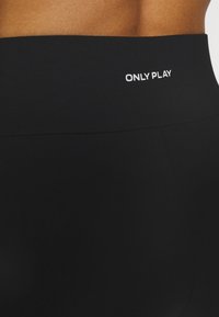 Svarta leggings har en bred, slät midja med texten "ONLY PLAY" i vitt. Tyget verkar elastiskt och kroppsnära.