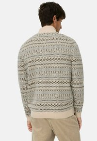 Beige gebreide trui met patronen, featuring een geribde kraag, geometrische ontwerpen in bruin en grijs, met een gestructureerde brei en aansluitende manchetten.