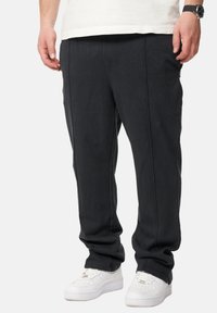 Schwarze Hose aus einem weichen Material mit lockerer Passform. Mit Vordernähten und Seitentaschen, kombiniert mit weißen Sneakern.