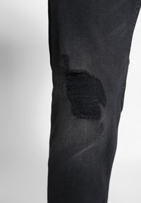 Mustat farkut, joissa on kulunut polvi, jossa on repsottavat reunat ja teksturoidulla paikalla korostettu käytetty ilme.