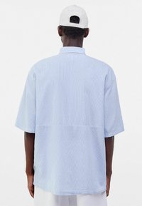 Světle modrá košile s krátkým rukávem a uvolněným střihem, texturovaná tkanina a s vertikálními pruhy, s límcem a rovnými lemy.