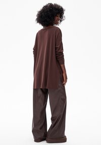 Bruine lange mouwtop met een relaxed fit en zijsplitten, gecombineerd met losse, donkerbruine lerenachtige broeken. Overal een soepele textuur.