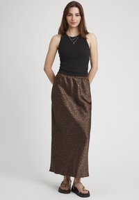 Un haut noir sans manches associé à une longue jupe en satin marron avec un motif léopard subtil. Des sandales complètent le look.