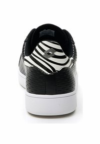 Black sneaker with textured upper, white sole, and a black and white striped heel. Features logo on the heel in a contrasting color.