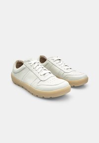 Sneakers bianchi in pelle con suole in gomma beige, caratterizzati da dettagli perforati, lacci piatti e una finitura liscia. Punta arrotondata e design a profilo basso.