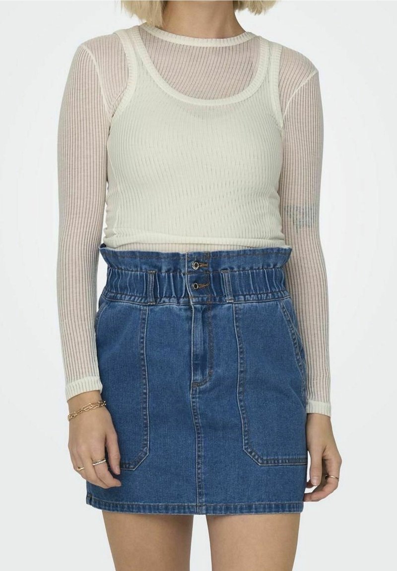 Top bianco a maniche lunghe a righe indossato sopra un top beige a righe, abbinato a una gonna di jeans blu scuro con vita elastica e tasche.