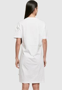 Biała bawełniana sukienka t-shirtowa z krótkimi rękawami, luźny krój i długość do bioder. Posiada minimalne detale szycia oraz tag z boku.