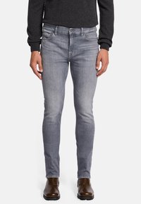 Jeans in denim skinny-fit grigio chiaro, con una leggera sfumatura, design a cinque tasche e zip frontale. Abbinati a stivaletti alla caviglia marroni.
