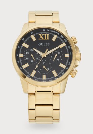 Gold-tone chronograph watch with black dial, silver index markers, three sub-dials, and a polished metal bracelet. Features tachymeter scale.