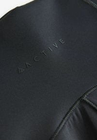 Crni aktivni materijal s teksturiranim šavovima i istaknutim logotipom koji kaže "ACTIVE". Glatka površina s oblikom koji se prilagođava tijelu.