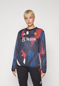 Langermet trøye laget av pustende stoff, med en marineblå base og abstrakte mønstre i rødt og blått, samt et Manchester United-logo.