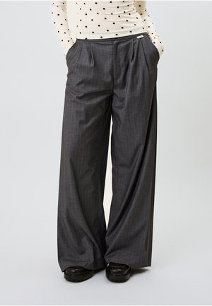 Graue, weit geschnittene Anzughose mit Längsstreifen, Falten, seitlichen Taschen und flacher Vorderseite. Hergestellt aus strukturiertem Stoff, kombiniert mit schwarzem Schuhwerk.
