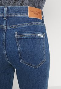 Dark blue denim jeans featuring a brown leather waistband label with "Marc O’Polo DENIM," classic back pockets, and contrasting stitching.