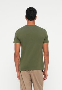 Tricou cu mânecă scurtă de culoare verde măsliniu, realizat dintr-un material moale, cu un decolteu clasic și o tăietură lejeră pe spate.