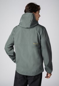 Hoodie van zacht, gedempt groen materiaal. Voorzien van een ritssluiting, elastische manchetten en een klein gouden logo op de achterkant.