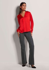 Rode satijnen blouse met lange mouwen en een diepe V-hals, gecombineerd met donkergrijze slim-fit jeans en zwarte puntige hakken. Soepele textuur en nauwsluitende pasvorm.