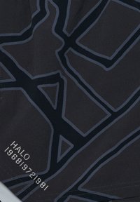 Čierna tkanina s geometrickým vzorom v tmavosivej farbe. Obsahuje malé biele písmo v dolnom ľavom rohu. Hladká textúra, ľahká konštrukcia.