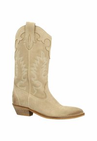 Beige suède cowboylaars met ingewikkelde witte stiksels en een gebogen bloemontwerp. Puntige neus en lage gestapelde hak. Accent trekstrip op de schacht.