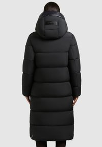 Longue doudoune noire avec capuche, présentant un design matelassé, une texture lisse et une fermeture éclair en bas. Détail du logo sur la capuche arrière.