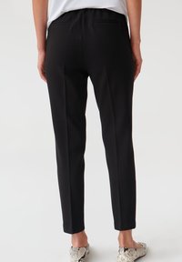 Svarta skräddarsydda byxor med en slät yta, med en elastisk midja, slim fit och två bakfickor. Matchat med mönstrade lägenheter.