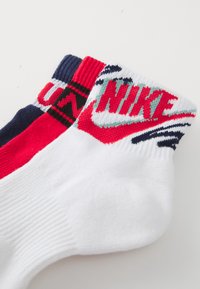 Vita, röda och marinblåa crew-strumpor med en ribbad design. Har Nike-logotyp i rött och teal, med kontrasterande mönster på kanten. Mjuk textur.