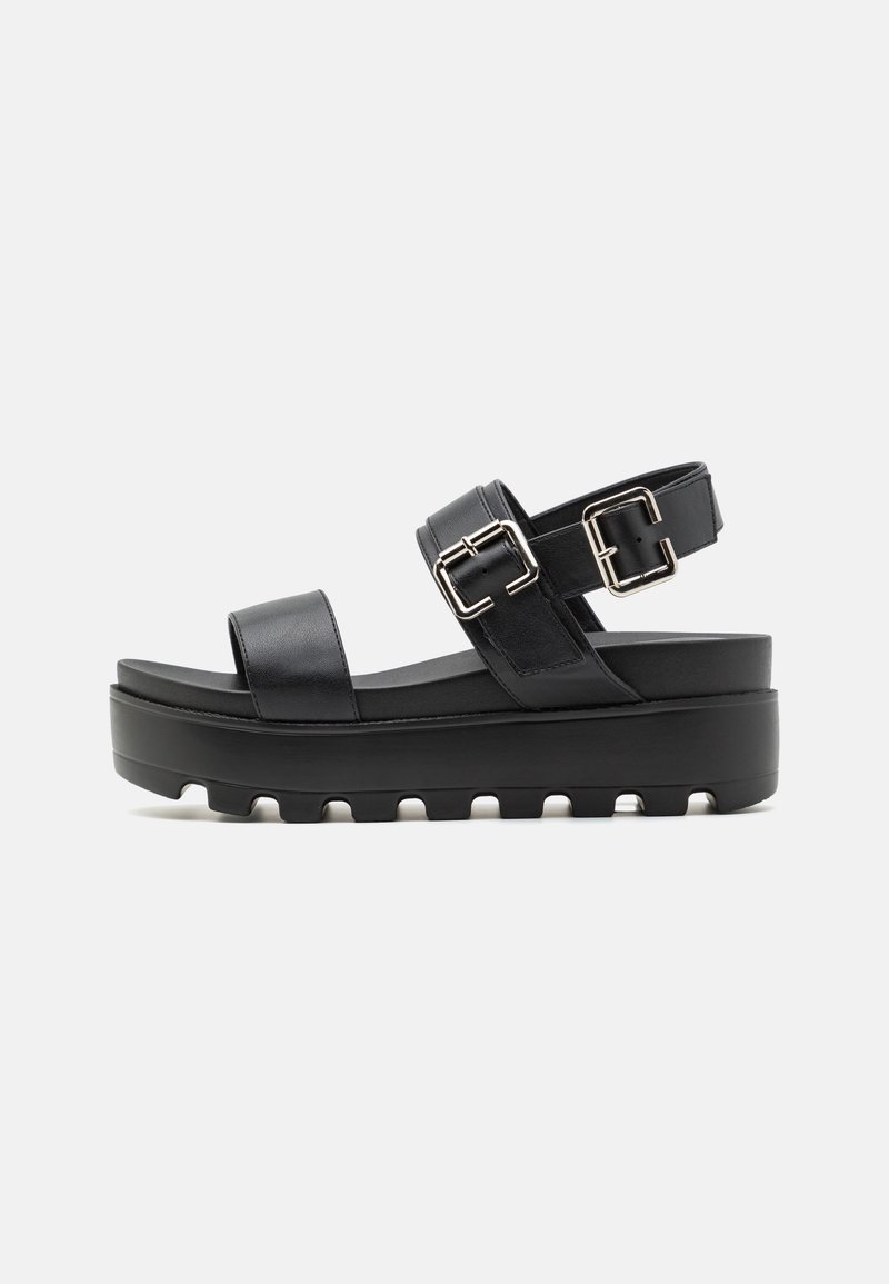 Black platform sandals feature a smooth leather upper with two adjustable straps and metal buckles. The sole is thick and textured for grip.