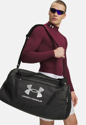Schwarz-graue Sporttasche mit großem silbernem Under Armour-Logo, strapazierfähigem Material, robusten Griffen und Reißverschlussverschluss.