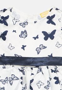 Valge kleit tumesiniste liblikamustritega ja ühetoonilise tumesinise vööga vöö ümber.