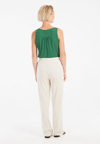 Top verde senza maniche in tessuto texturizzato, abbinato a pantaloni larghi color crema. Vita visibile e design a gamba dritta.
