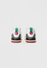 Buty sportowe z białą siateczką, czarnymi teksturowanymi akcentami, czerwonymi detalami i zielonym uchwytem pięty z okrągłym logo.