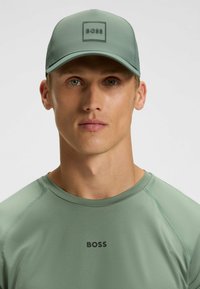 Lichtgroene pet met een gestructureerde vierkante logopatch. Glad fabric en gebogen klep. Gecombineerd met een bijpassende lichtgroene shirt met een logo.