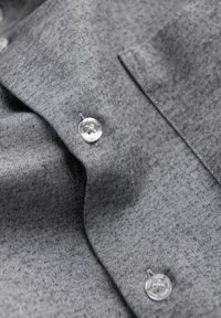 Chemise grise à boutons avec un tissu texturé, présentant un col plié, des boutons visibles et de légères rayures diagonales.