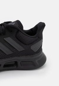 Scarpa da ginnastica nera con parte superiore in mesh, tre strisce laterali prominenti, collare imbottito e suola in gomma testurizzata perUna migliore aderenza.