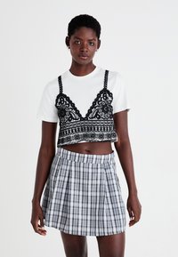 Top corto de encaje negro con detalles intrincados, superpuesto a una camiseta blanca sencilla. Combinado con una falda mini de cuadros con pliegues en gris y negro.